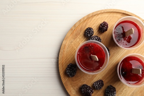 Tasty berry ice pops in plastic cups and space for text on white wooden table, top view. Fruit popsicle