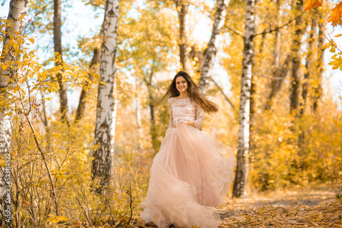 girl in a long light Peach Fuzz  puffy dress runs through the autumn birch