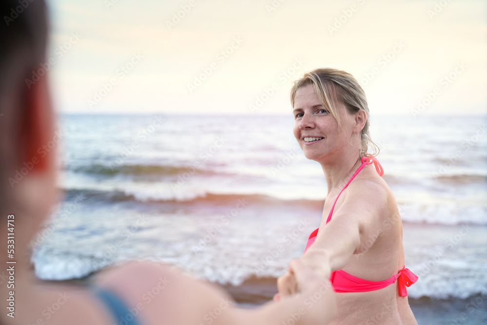 follow me swimming. Smiling girl standing at sea and invites you to swim, follow me travel concept. Young woman in follow me pose enjoying the summer.