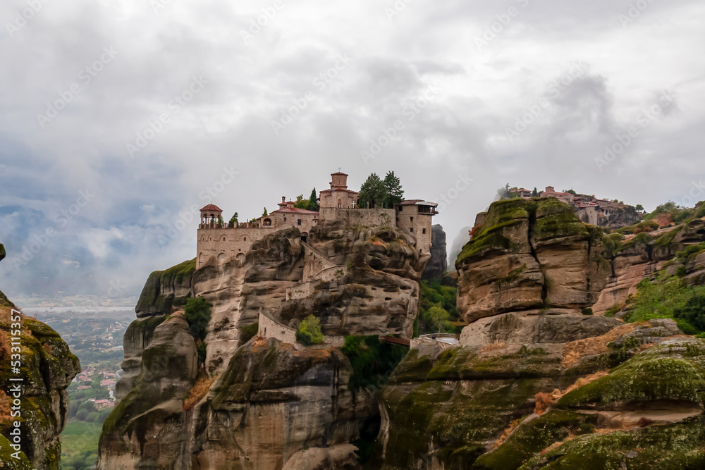 Scenic view of Holy Monastery of Varlaam on cloudy foggy day, Kalambaka, Meteora, Thessaly, Greece, Europe. Rock formations overgrown with green moss creating moody atmosphere. UNESCO World Heritage Scenic view of Holy Monastery of Varlaam on cloudy foggy day, Kalambaka, Meteora, Thessaly, Greece, Europe. Rock formations overgrown with green moss creating moody atmosphere. UNESCO World Heritage