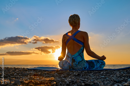 Young woman practicing yoga on the beach at sunrise. Harmony, wellbeing, meditation, healthy lifestyle, relaxation, yoga, self care, mindful meditation concept.