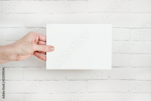 hand holds white blank form against brick wall. Copy space, text space. Layout template, information