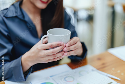 Portrait of a happy Asian woman smiling at her desk during the daytime coffee break