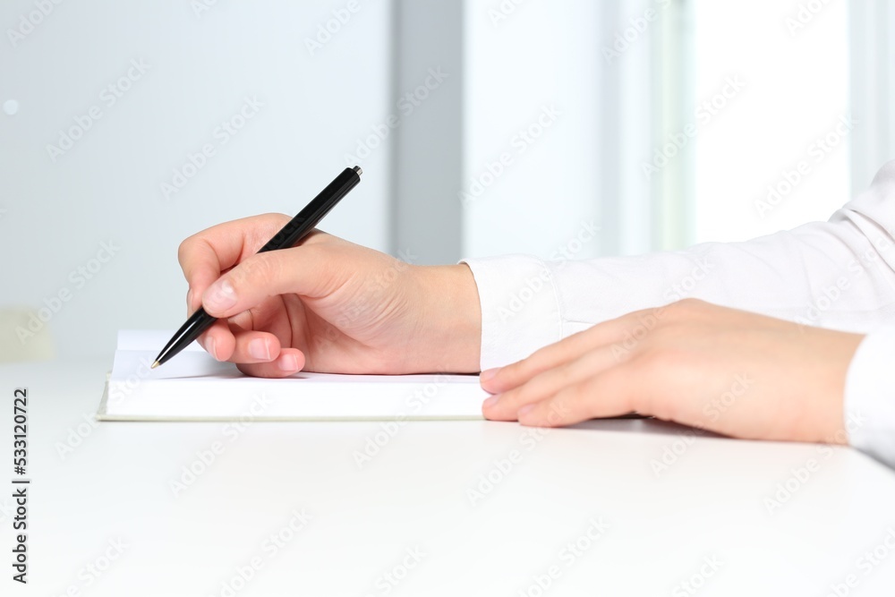 Woman writing in notebook at white table in office, closeup Woman writing in notebook at white table in office, closeup
