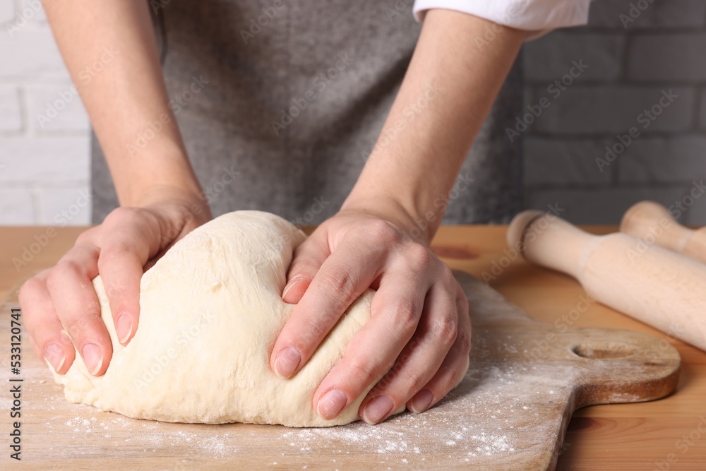 Woman kneading dough at wooden table near white brick wall, closeup Woman kneading dough at wooden table near white brick wall, closeup