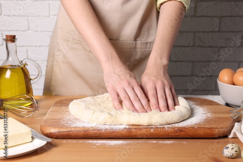 Woman kneading dough at wooden table near white brick wall, closeup © New Africa