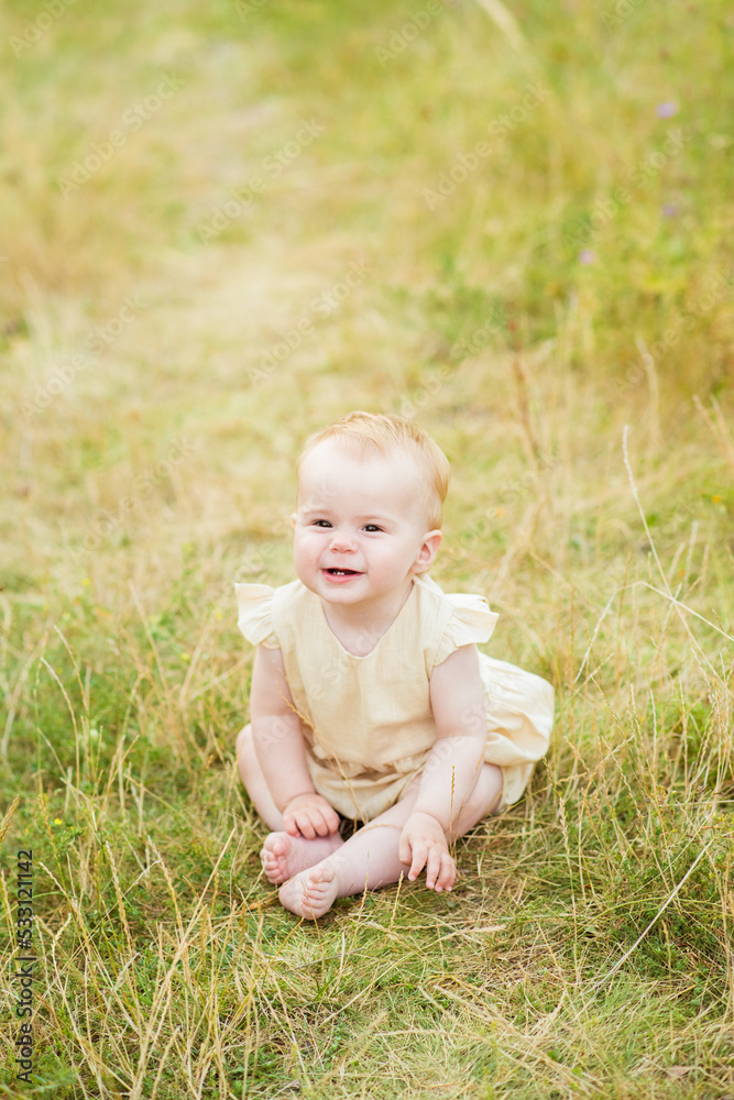 Happy baby girl sitting on the grass in field. Autumn nature