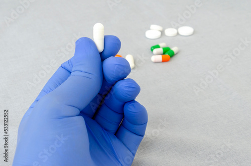 Medication pills in hand of doctor or nurse. Capsule pill on grey background. Nitrile disposable gloves and medicines. Drugs healthcare treatment. Medical concept