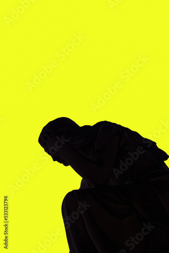 Statue shadow silhouette of an angel holding head with hand, against a strong yellow background. © bestravelvideo