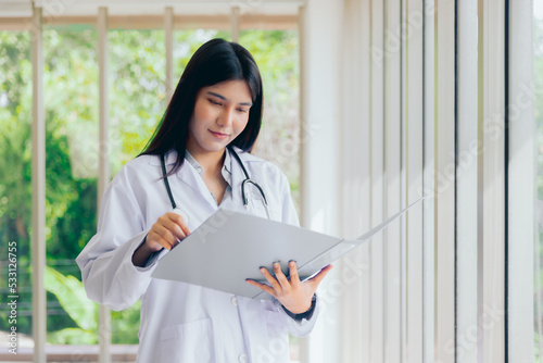 Asian young woman doctor checking patient's medical records folder or prescription with medical staff working on the background,Portrait doctor healthcare professionals
