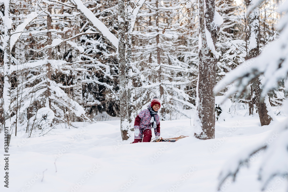 Happy little African-American girl in a red hat and jumpsuit rides on tubing in the winter park.Beautiful trees are covered with white snow.Winter fun,active lifestyle concept.