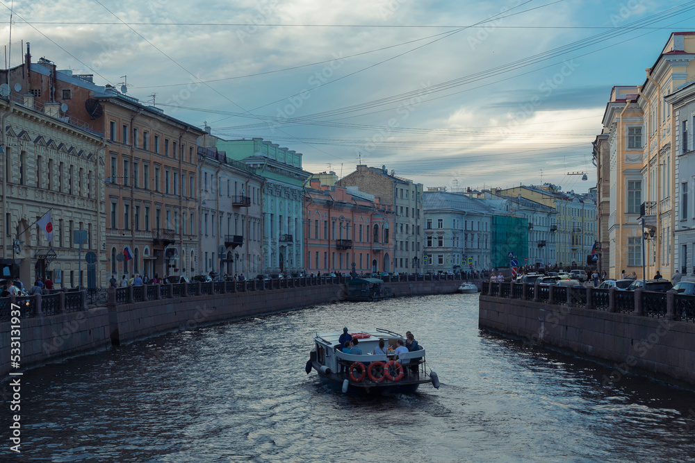 Obraz premium A boat on a river surface against people on an embankment and a Saint Petersburg cityscape by summer day