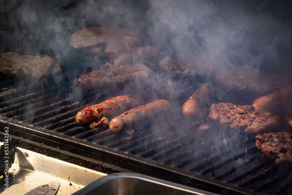 Sausages and hamburger cutlets are fried in smoke on a grill grate Sausages and hamburger cutlets are fried in smoke on a grill grate