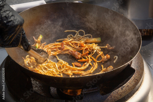 Cooking noodles with meat and vegetables in a deep wok over an open fire. street food