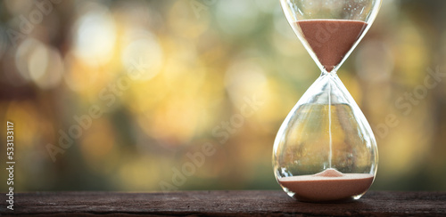 Photos hourglass (sand clock) on an old wooden table with natural blur background, Hourglass as time passing concept for business deadline, Life-time passing concept, elapsed time concept, copy space