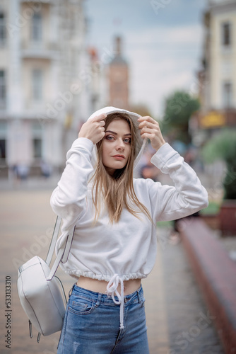 a girl in a white sweater is walking around the city