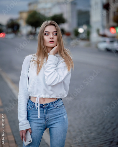 a girl in a white sweater is walking around the city