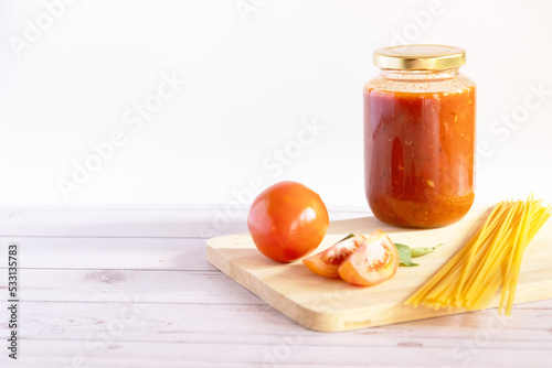 Homemade tomato sauce and ketchup in a glass jar on the table with fresh ingredients photo