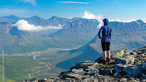 Female hiker in blue jacket overlooking vast arctic mountain landscape from the top of the mountain. Top of Naite, Sarek National Park, Sweden. Hiking in Lapland. Outdoor adventure in the arctic. photo