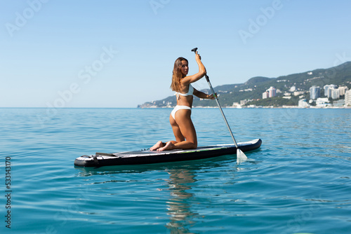 A young fit sexy woman in a swimsuit poses with a sup board. Rear view. Sup surfing. © Artem Zakharov