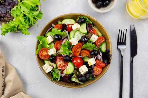 Fresh greek salad with cherry tomato, cucumber, lettuce, black olive, feta cheese and olives oil on gray concrete background. 
