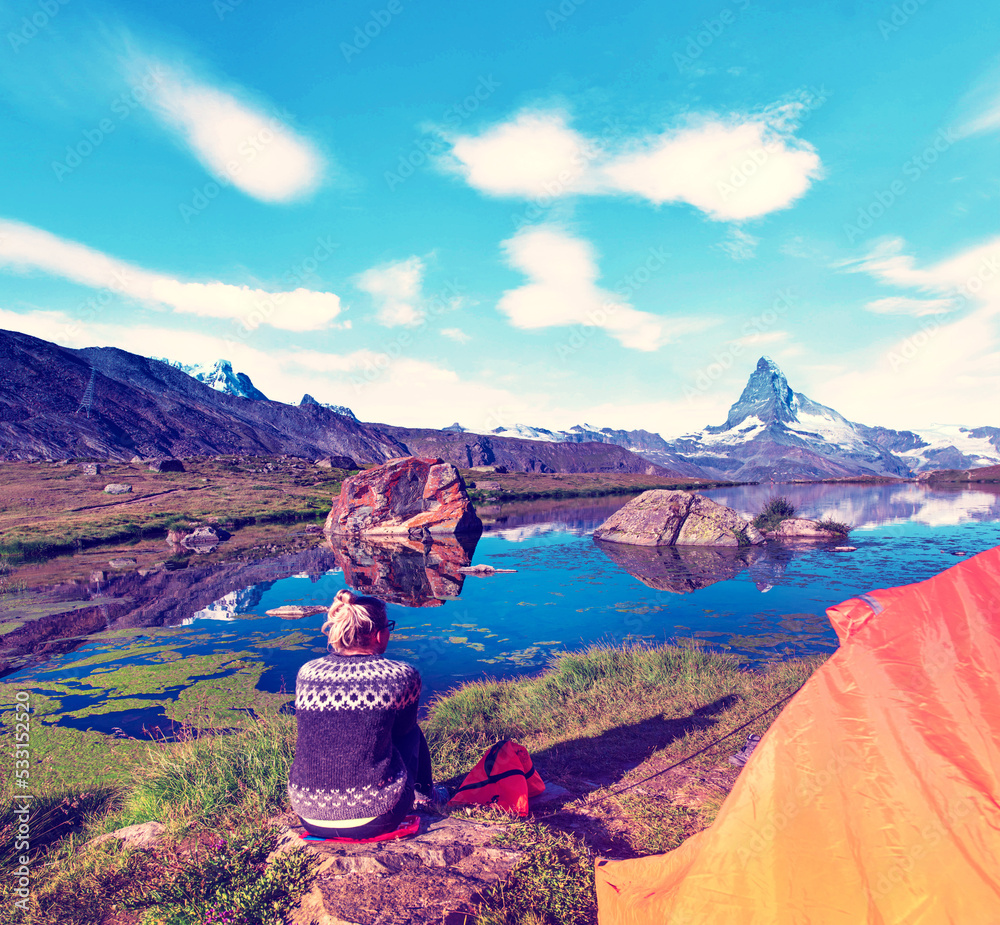 A young girl near tent looks at a fantastic mountain landscape with Matterhorn in the Swiss Alps, near Zermatt, Switzerland