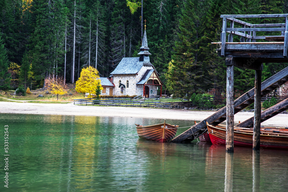 charming fascinating autumn landscape with a church and boats on the lake on Fanes-Sennes-Braies natural park in the Dolomites in South Tyrol, Alps, Italy.