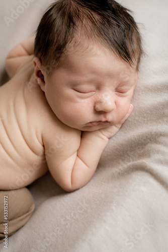 A cute little baby in cute pants sleeps on a beige textile bedspread. Health and motherhood