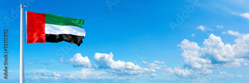 United Arab Emirates flag waving on a blue sky in beautiful clouds - Horizontal banner