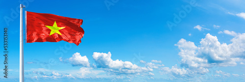 Billede på lærred Vietnam flag waving on a blue sky in beautiful clouds - Horizontal banner