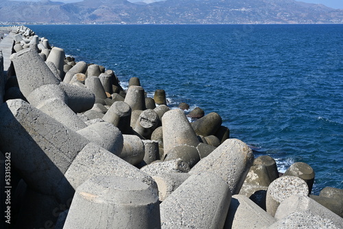 Close view on concrete tetrapod breakwater stones piled up in wave breaker to protect Port of Heraklion, North Crete, from waves of Mediterranean Sea. In horizon is coastline of Greek island.
