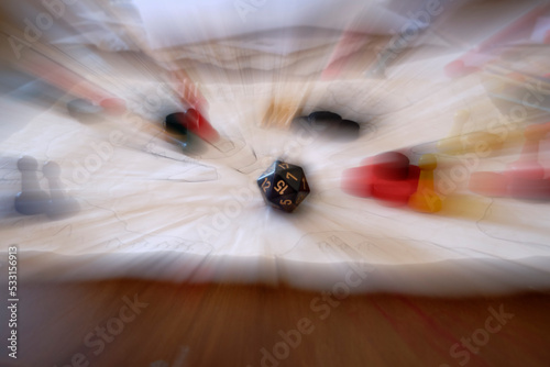 Optical zoom technique, blurred motion zoom centering on a black 20 sided dice (d20) on a role paying game table, along with hand drawn map, papers and other role play game pieces.