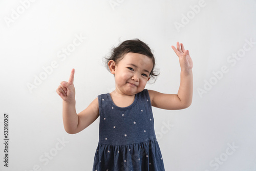 Happy smiling Asian child girl posing and pointing up isolated on white background.