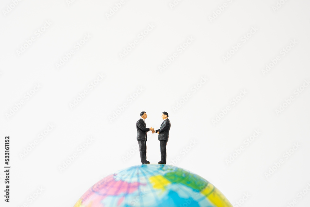business miniature people shaking hands on world ball toy on white background business miniature people shaking hands on world ball toy on white background