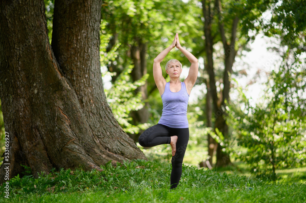 Middle aged woman practicing yoga outdoors in tree pose.Going in for sports in the city park.