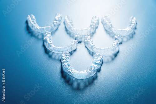 invisible plastic braces lie in reverse inverted pyramid shape in a row on a blue background, studio shot, nobody