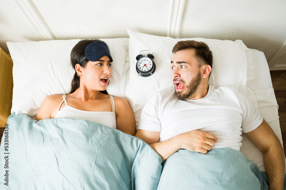 Stressed couple waking up late in bed with an alarm clock Stressed couple waking up late in bed with an alarm clock
