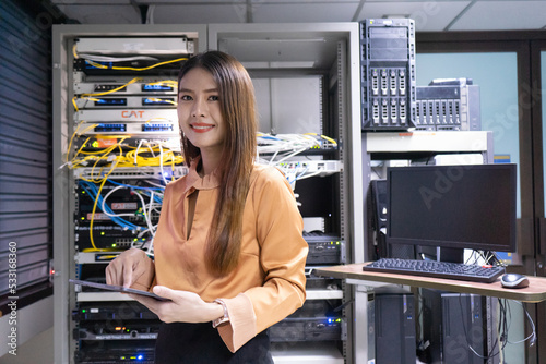 Portrait of young woman wearing glasses using digital tablet standing against server cabinets in data center