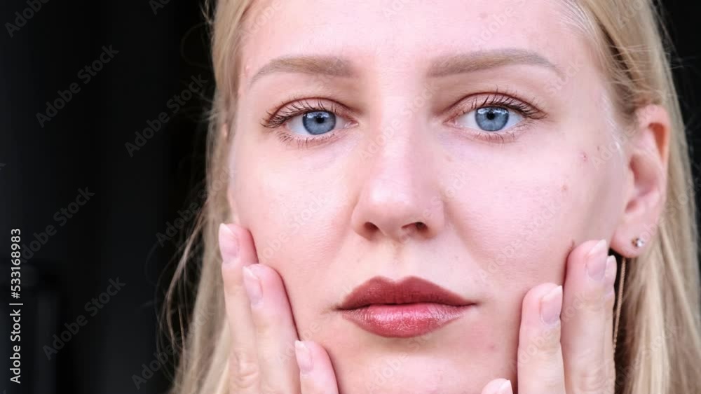 Close-up of beautiful woman's face. Young blue-eyed blonde girl touches her face looking at camera. Anti-aging care for common face and body. Prolongation of youth and freshness of the skin. Close-up of beautiful woman's face. Young blue-eyed blonde girl touches her face looking at camera. Anti-aging care for common face and body. Prolongation of youth and freshness of the skin.