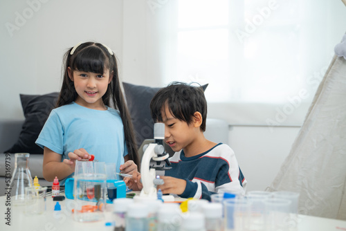 Two little scientists making chemical test with toy microscope in living room