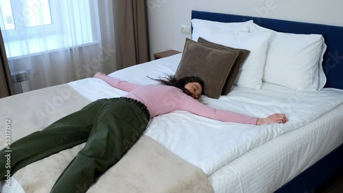 Young happy woman on vacation jumping and falling on the bed with a run in the hotel room in slow motion. She lies on the bed and smiles. The concept of rest and vacation. photo