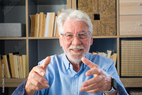 Head shot portrait confident old businessman coach wearing glasses looking at camera and talking, mentor speaker holding online lesson, explaining, sitting at wooden work desk in modern cabinet. photo