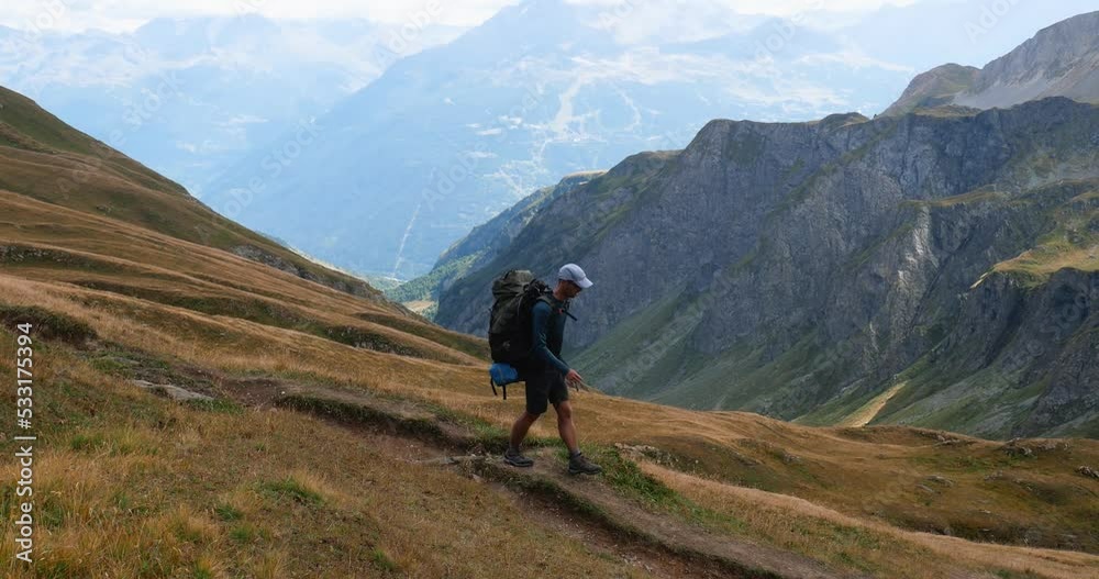 Man with a backpack hiking on a trail of the Alps moutains in summer, evocation of outddoors, freedom, trekking Man with a backpack hiking on a trail of the Alps moutains in summer, evocation of outddoors, freedom, trekking