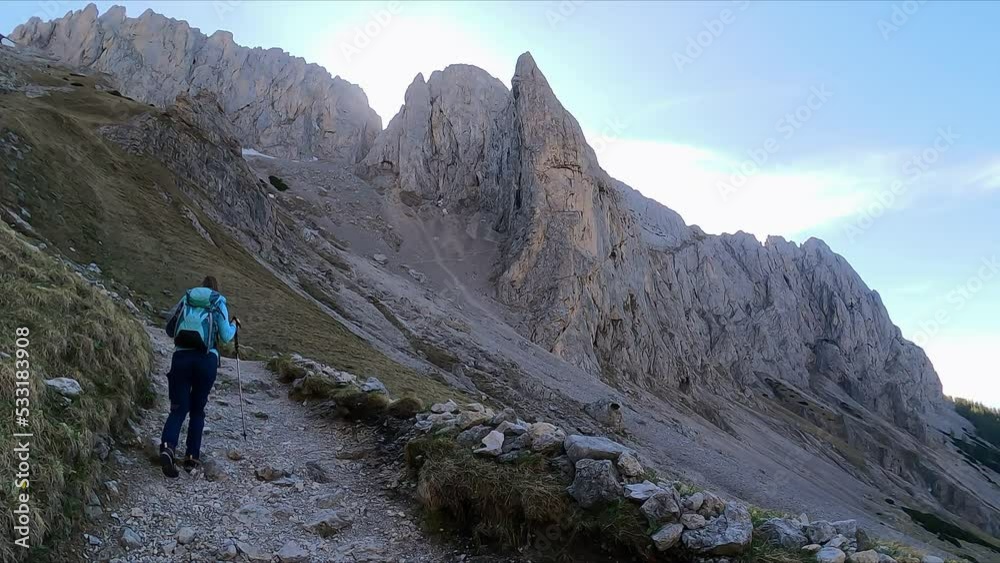 Rear view of woman with backpack on hiking trail surrounded by massive steep mountain peaks in Hochschwab Alps, Upper Styria, Austria, Europe. Hiking route through Foelzklamm to Foelzstein, Foelzkogel Rear view of woman with backpack on hiking trail surrounded by massive steep mountain peaks in Hochschwab Alps, Upper Styria, Austria, Europe. Hiking route through Foelzklamm to Foelzstein, Foelzkogel