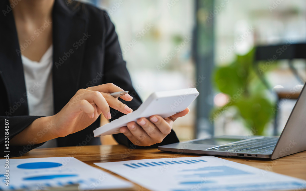 Asian female finance businessmen are calculating Investment results by calculator, Company performance from graph documents On desk in his office, business ideas for calculating investment results.