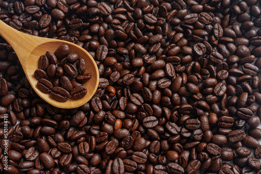 Roasted Coffee beans on wooden spoon with roasted coffee beans background Roasted Coffee beans on wooden spoon with roasted coffee beans background