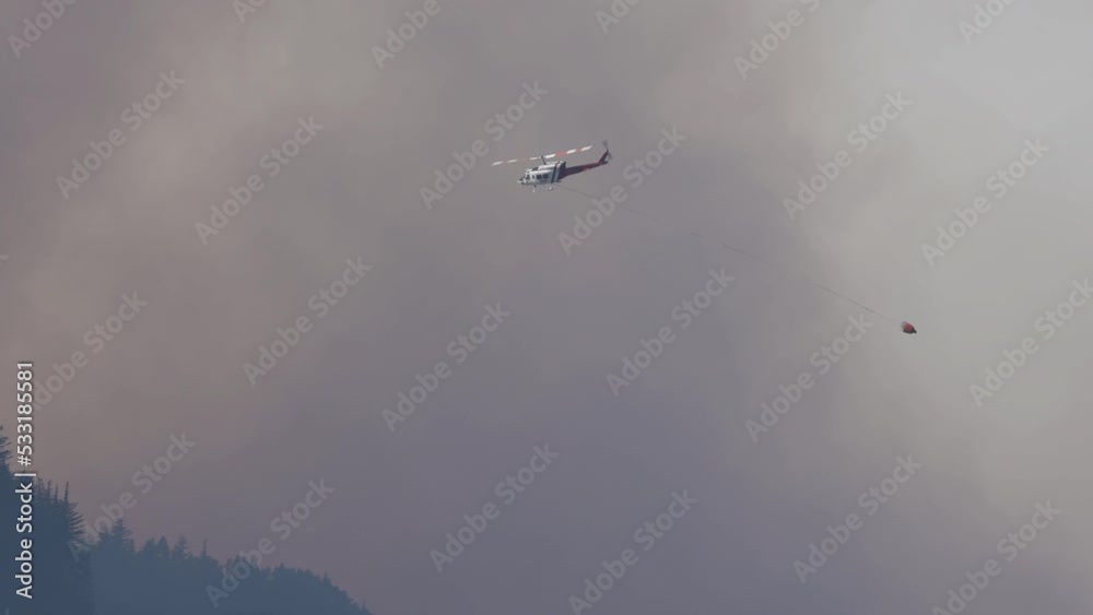 Wildfire Service Helicopter flying over BC Forest Fire and Smoke on the mountain near Hope during a hot sunny summer day. British Columbia, Canada. Natural Disaster Wildfire Service Helicopter flying over BC Forest Fire and Smoke on the mountain near Hope during a hot sunny summer day. British Columbia, Canada. Natural Disaster