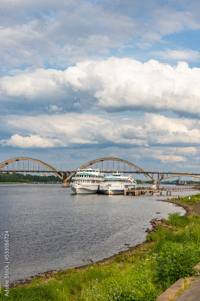 RYBINSK, RUSSIA - JULY 9, 2022: Volzhskaya embankment with cruise ships and Rybinsky bridge. Provincial russian city in summer day.