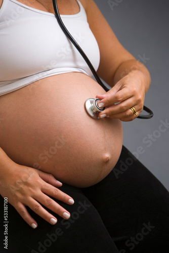 Pregnant woman checking her own belly with stethoscope