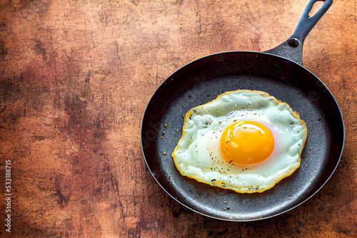 fried eggs, scrambled eggs in a frying pan with seasonings and spices, on a wooden table, close-up, rustic style, farm